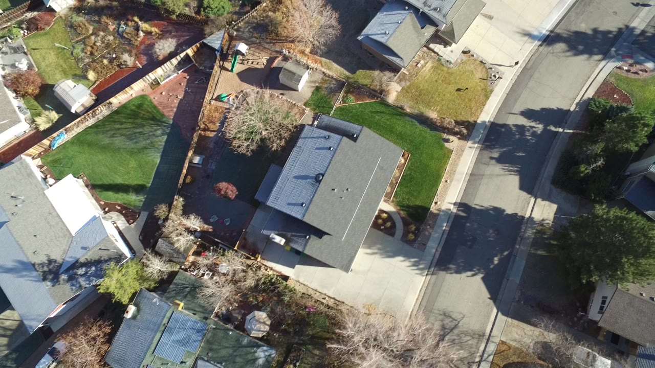 Aerial frame over Westminster, Colorado with several detached homes, paved driveways, lawns, bare trees, and a curving residential street, with no visible people.
