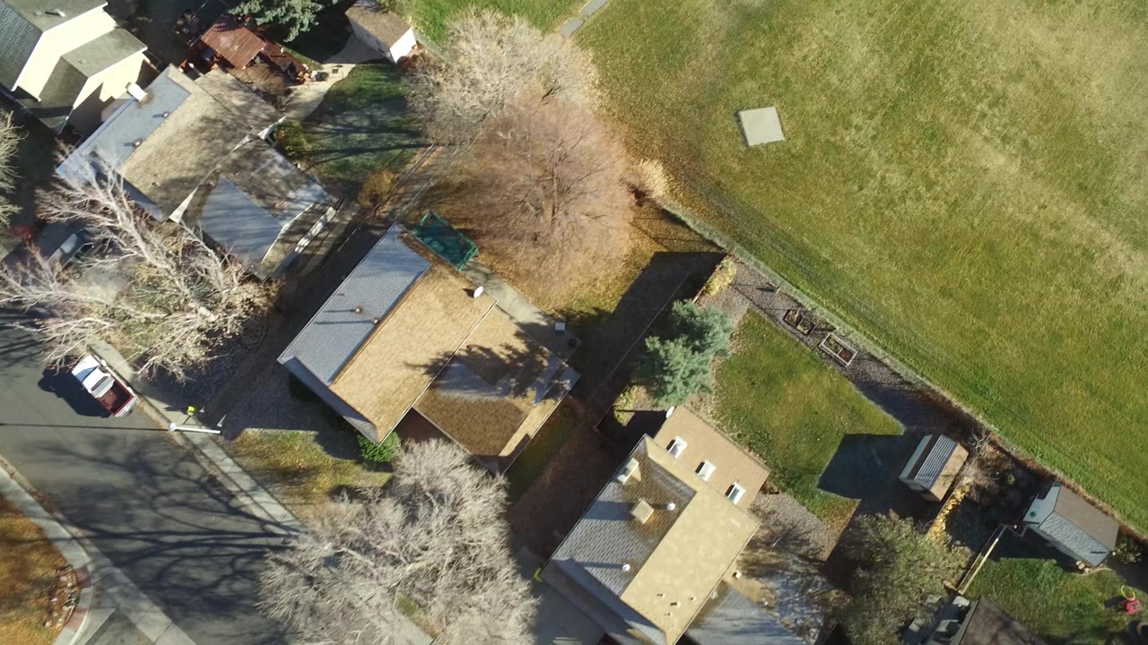 Overhead Westminster, Colorado view with several private homes along the lower left, a wide grass field to the right, tree shadows, and no visible people.