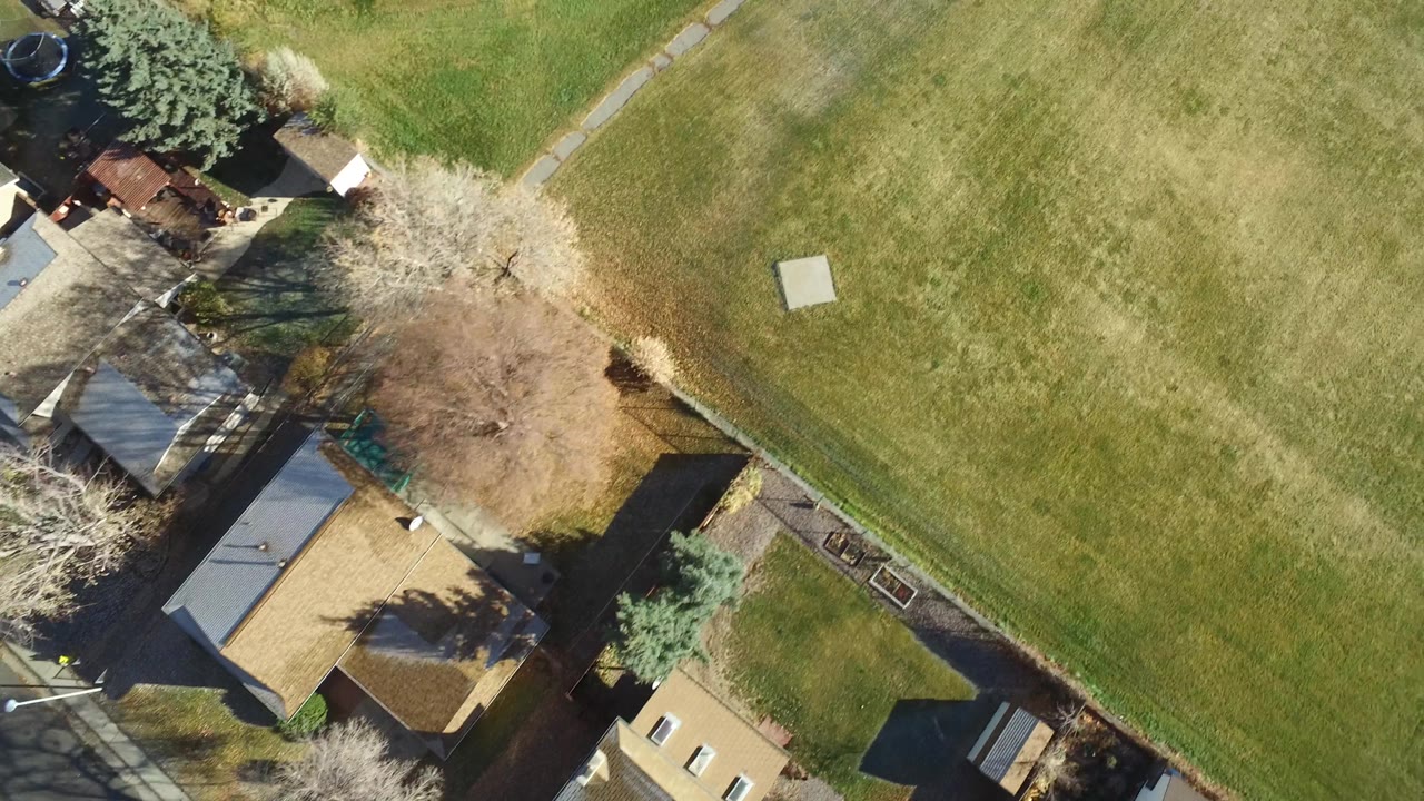 Aerial view shifting toward open grass with houses at the edge.