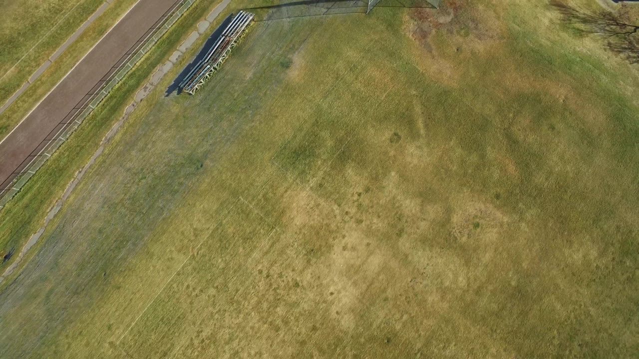 Grass field from above with bleachers and a sports fence visible.