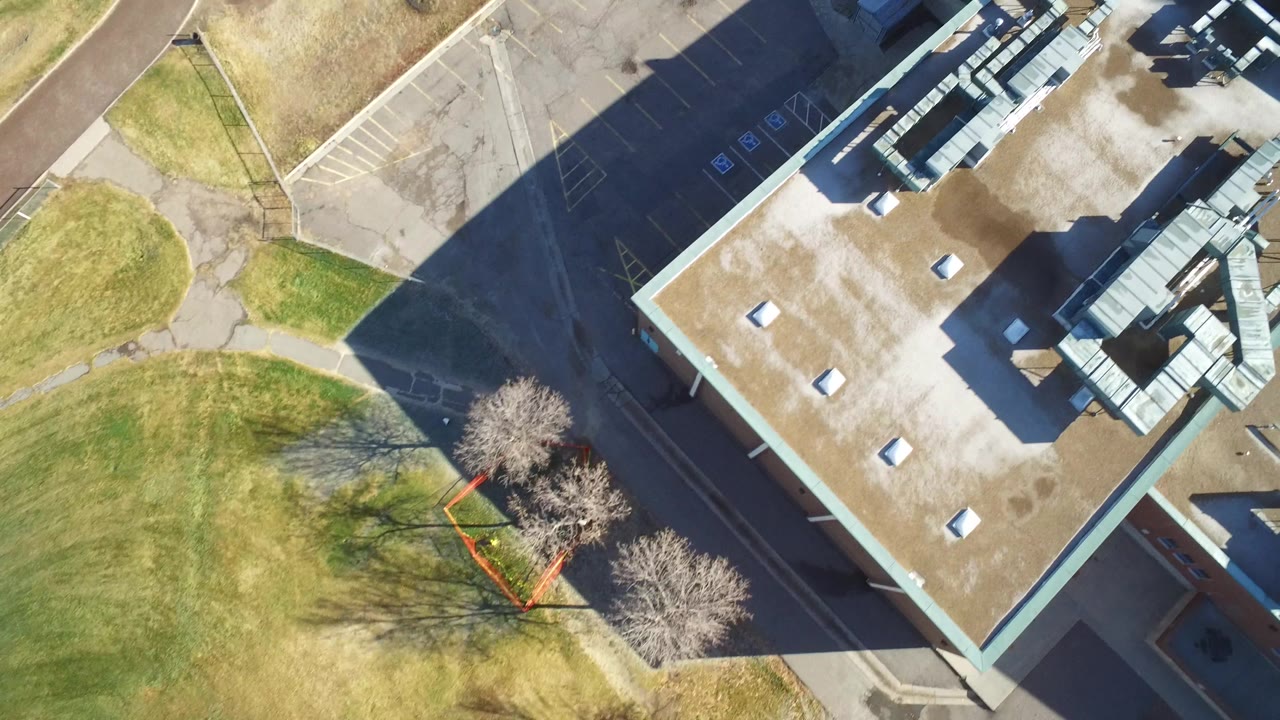 Overhead Westminster, Colorado view with more of the roof and HVAC structures visible, bordered by grass, sidewalks, parking spaces, tree shadows, and no visible people.