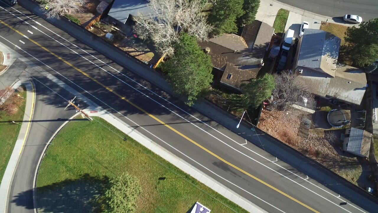 Overhead view of a suburban road, lawns, trees, and rooftops.