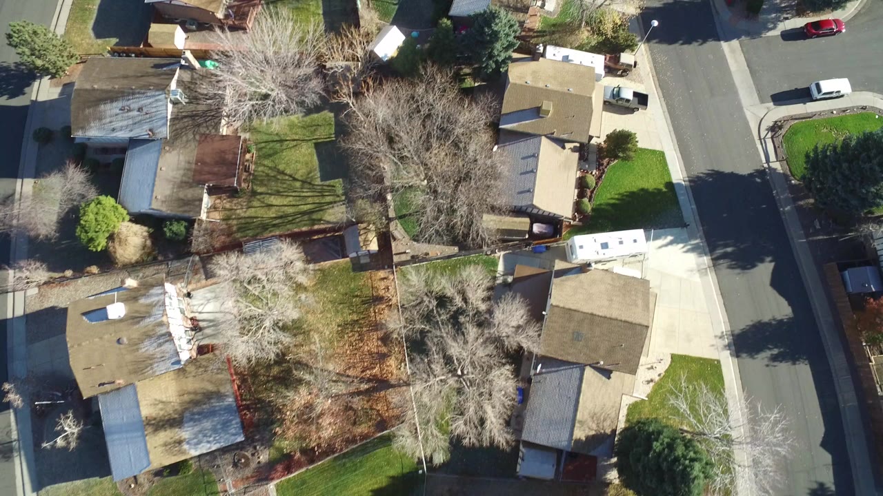 Overhead aerial frame of Westminster, Colorado homes, fenced yards, leafless trees, driveways, and a residential street, with no visible people discernible.