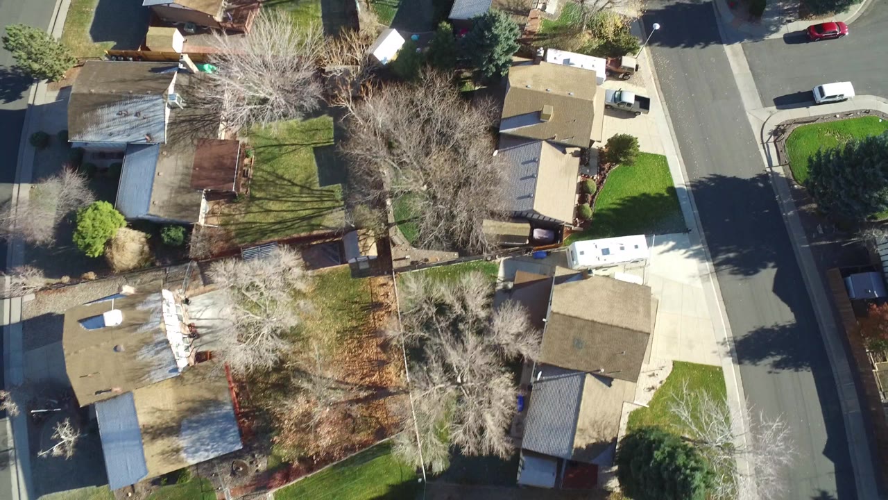 Aerial view of rooftops, lawns, parked vehicles, and a curved residential street.