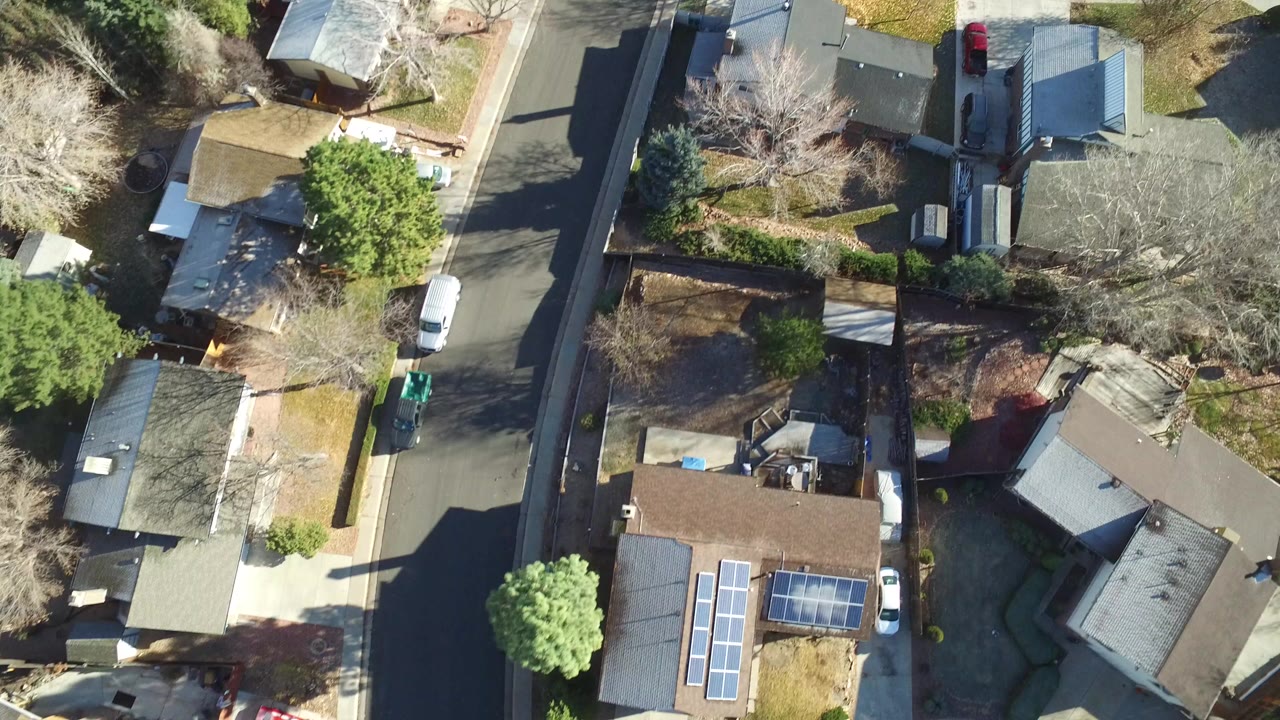 Overhead view of a Westminster, Colorado residential block with rooftops, a narrow street, driveways, winter-bare trees, evergreens, parked vehicles, and no visible people.