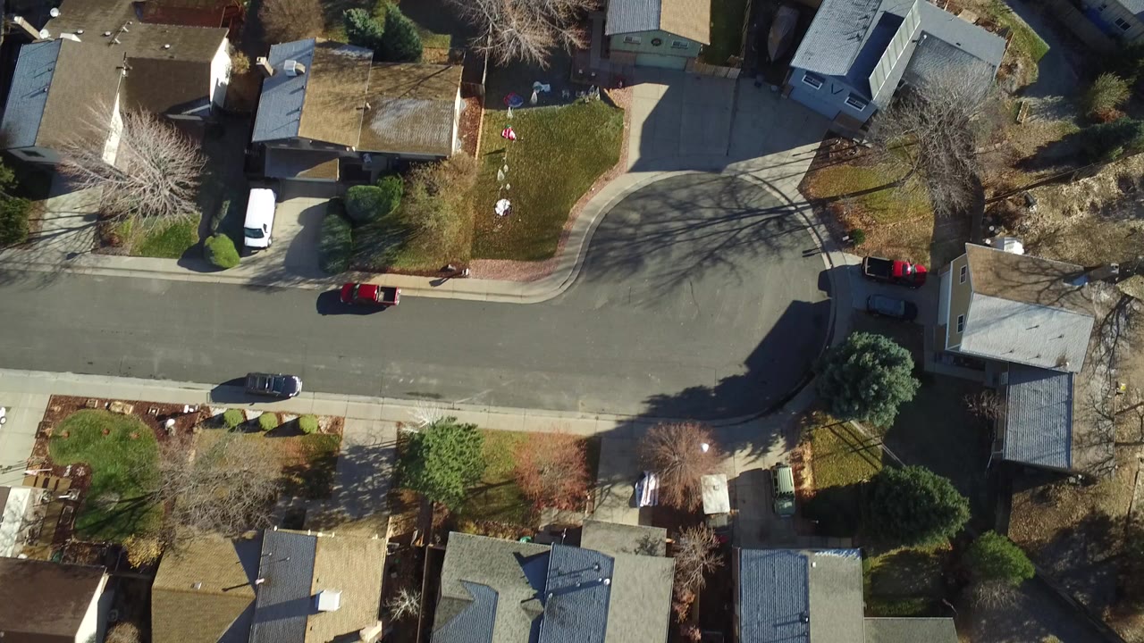 Overhead drone frame of Westminster, Colorado showing single-family homes, a curved residential street, driveways, lawns, leafless trees, parked cars, and no clearly visible people.