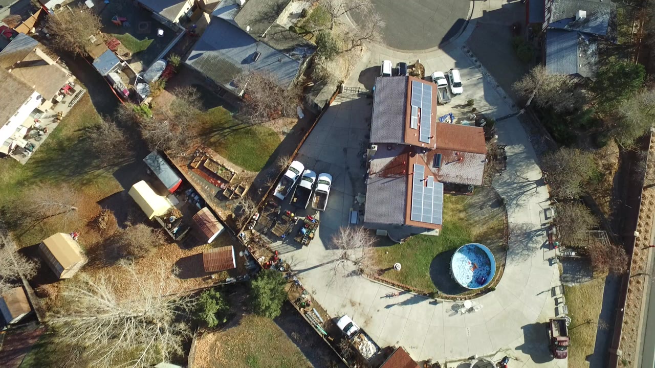 Overhead view of houses, driveways, cars, lawns, and a blue round pool.