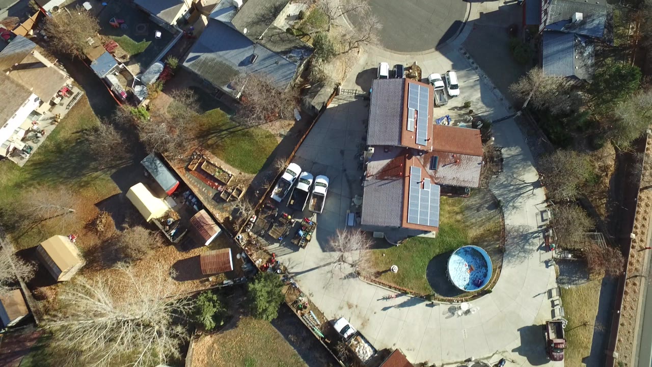 Overhead Westminster, Colorado view with a roof fitted with solar panels, nearby parked cars, fenced yards, trees, and a blue round pool with no visible people.