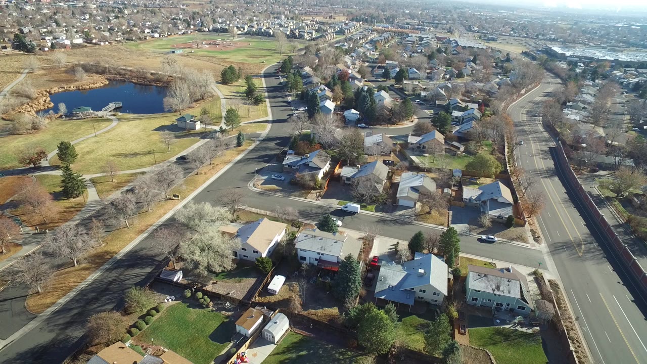 Aerial view of suburban homes beside a wide road and small pond.