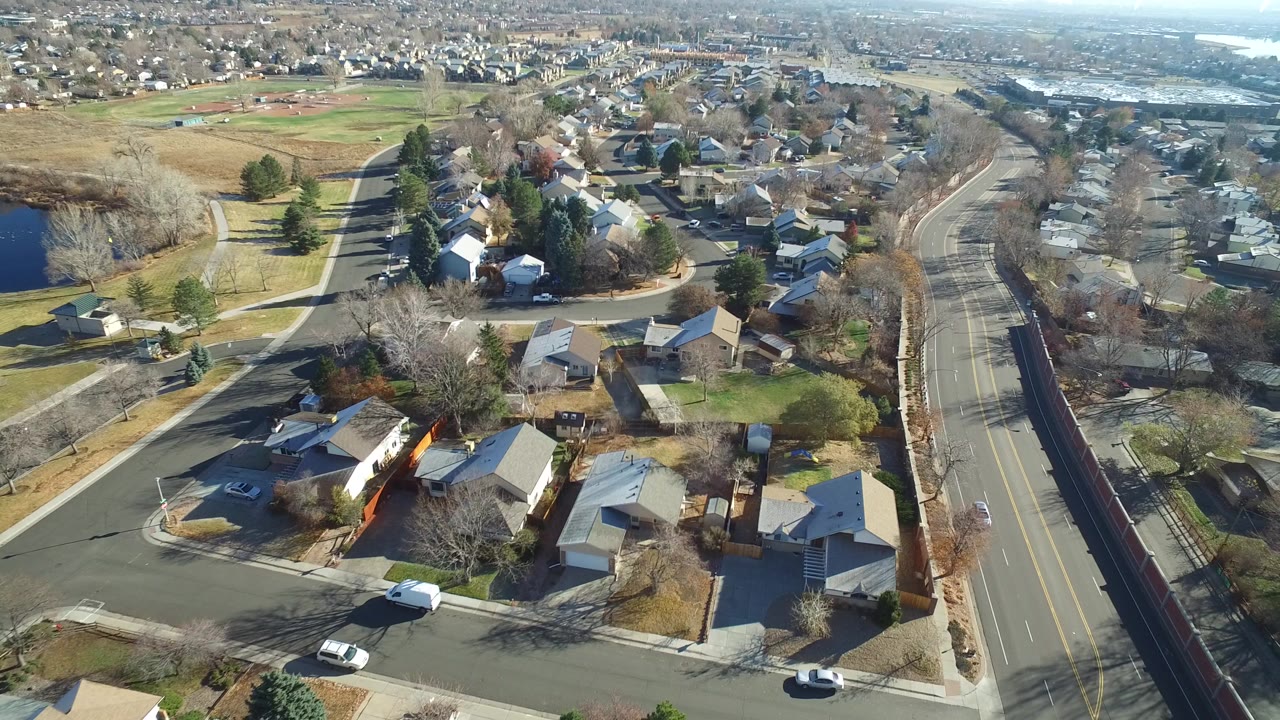 Aerial view of suburban houses, roads, lawns, and distant water.