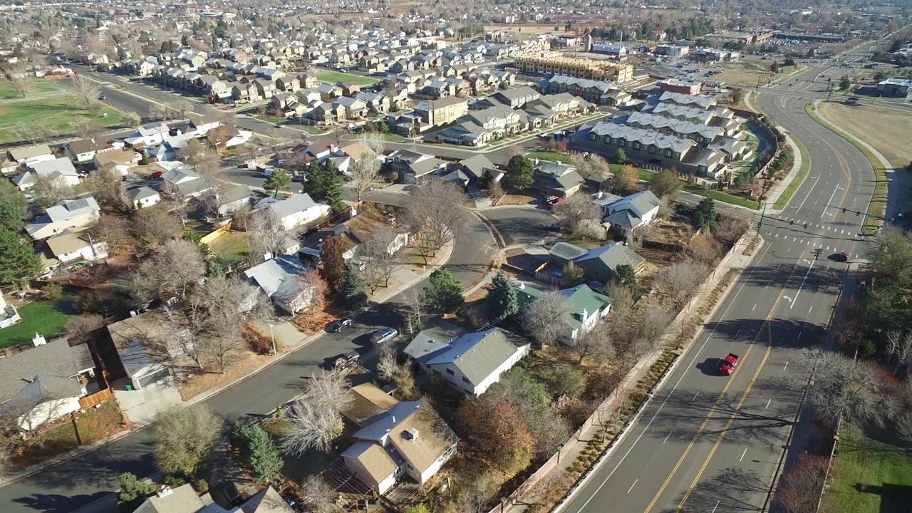 A high drone frame over Westminster, Colorado showing a residential intersection, rows of houses, cars on the road, and no visible people.
