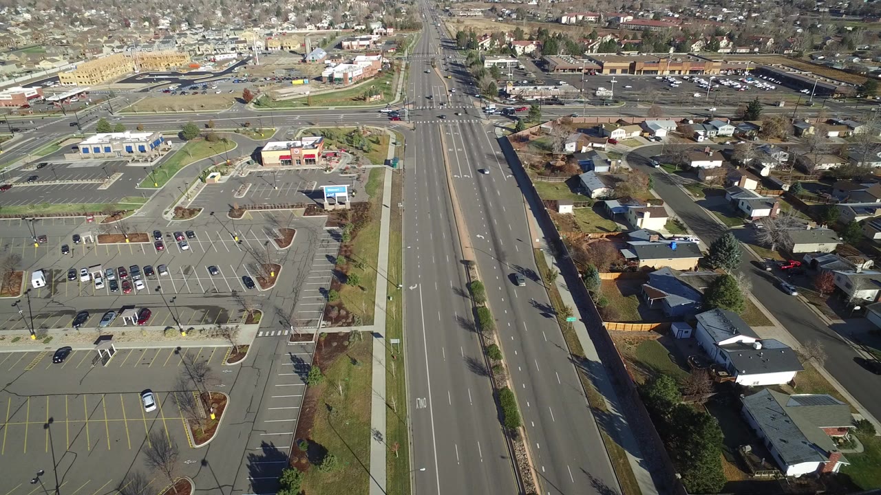 Aerial view of a multilane road beside parking lots and homes.