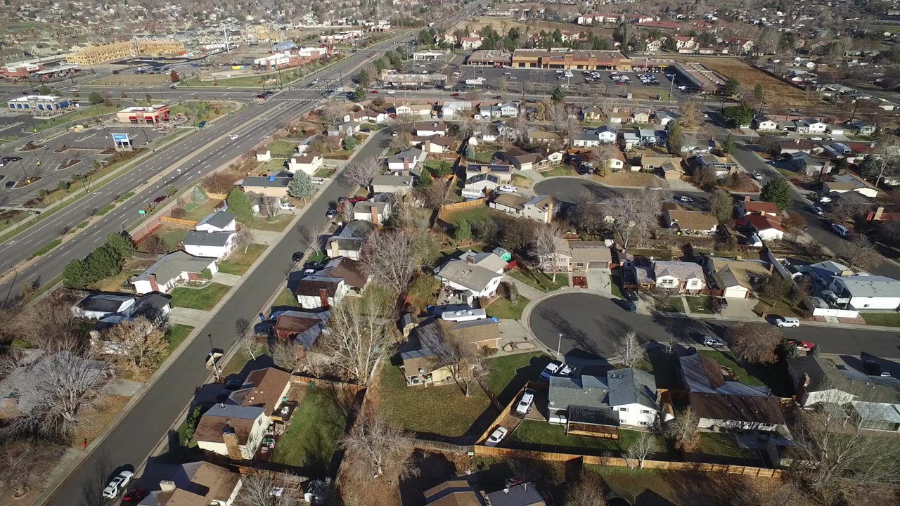 Aerial view over suburban houses, yards, roads, and leafless trees.