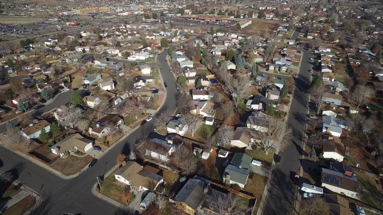 The aerial view over Westminster, Colorado includes intersecting asphalt roads, rows of rooftops, fenced backyards, scattered cars, and no visible people.