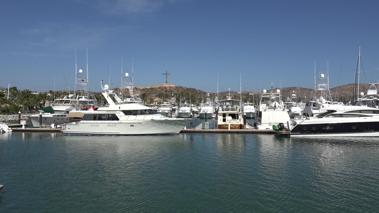 Yachts docked across calm marina water under a blue sky.