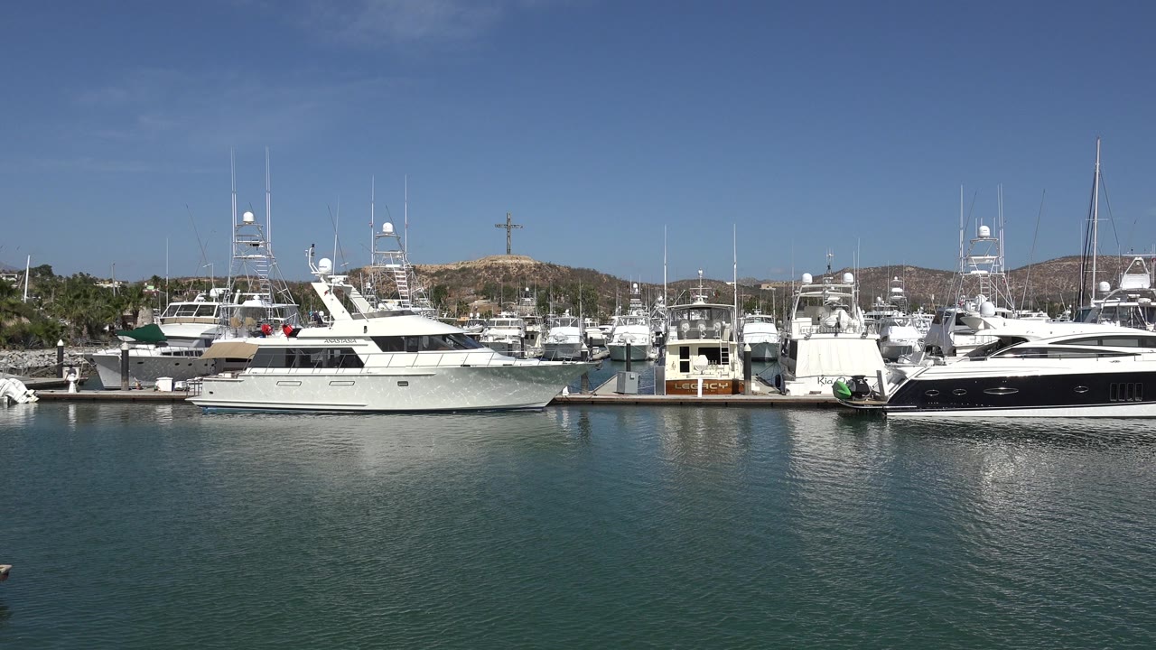 Yachts docked across blue-green harbor water under clear sky.