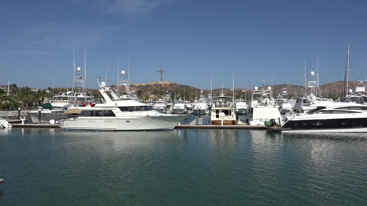 San Jose Del Cabo marina view with a large white yacht left of center, a dark-hulled yacht to the right, rippled water, and no visible people.