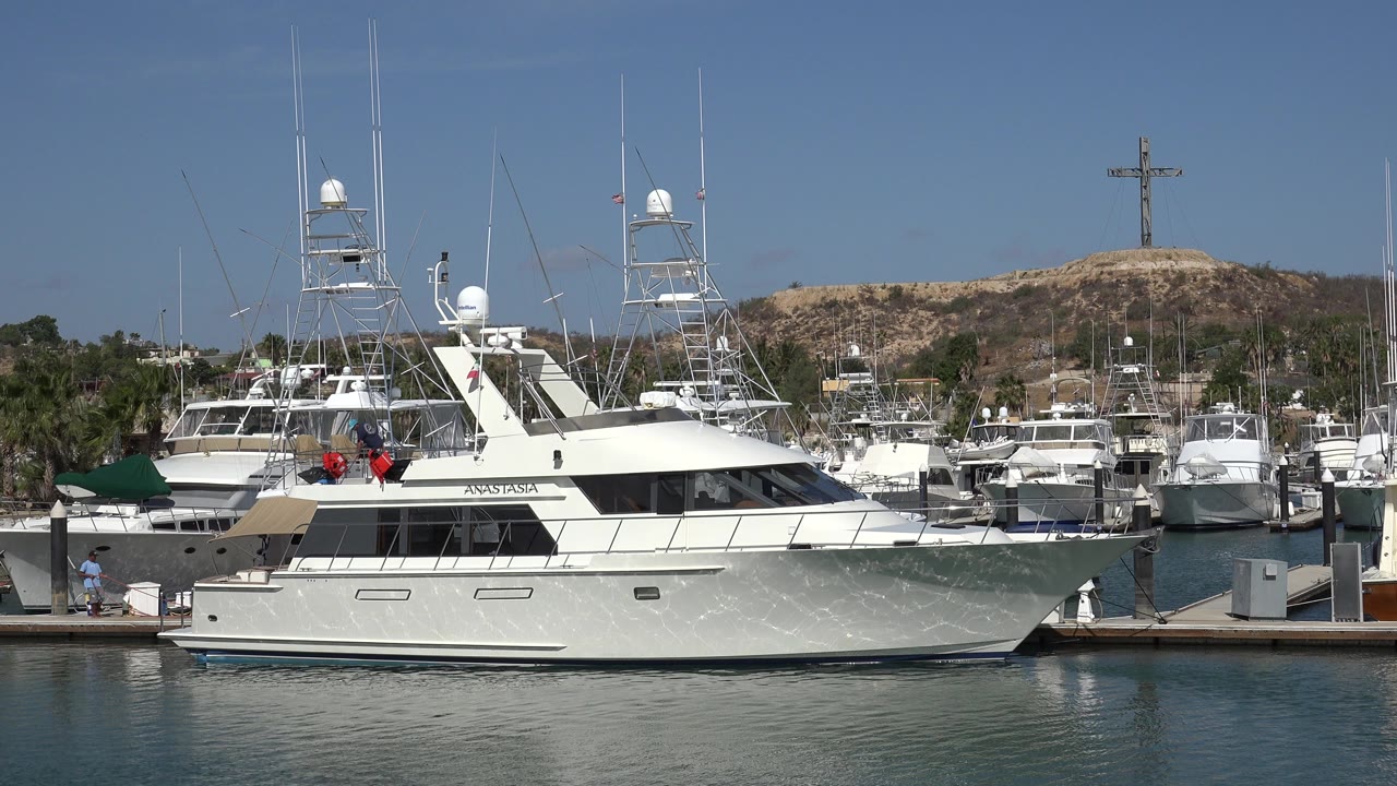 White yacht docked in a marina with water and hillside behind it.