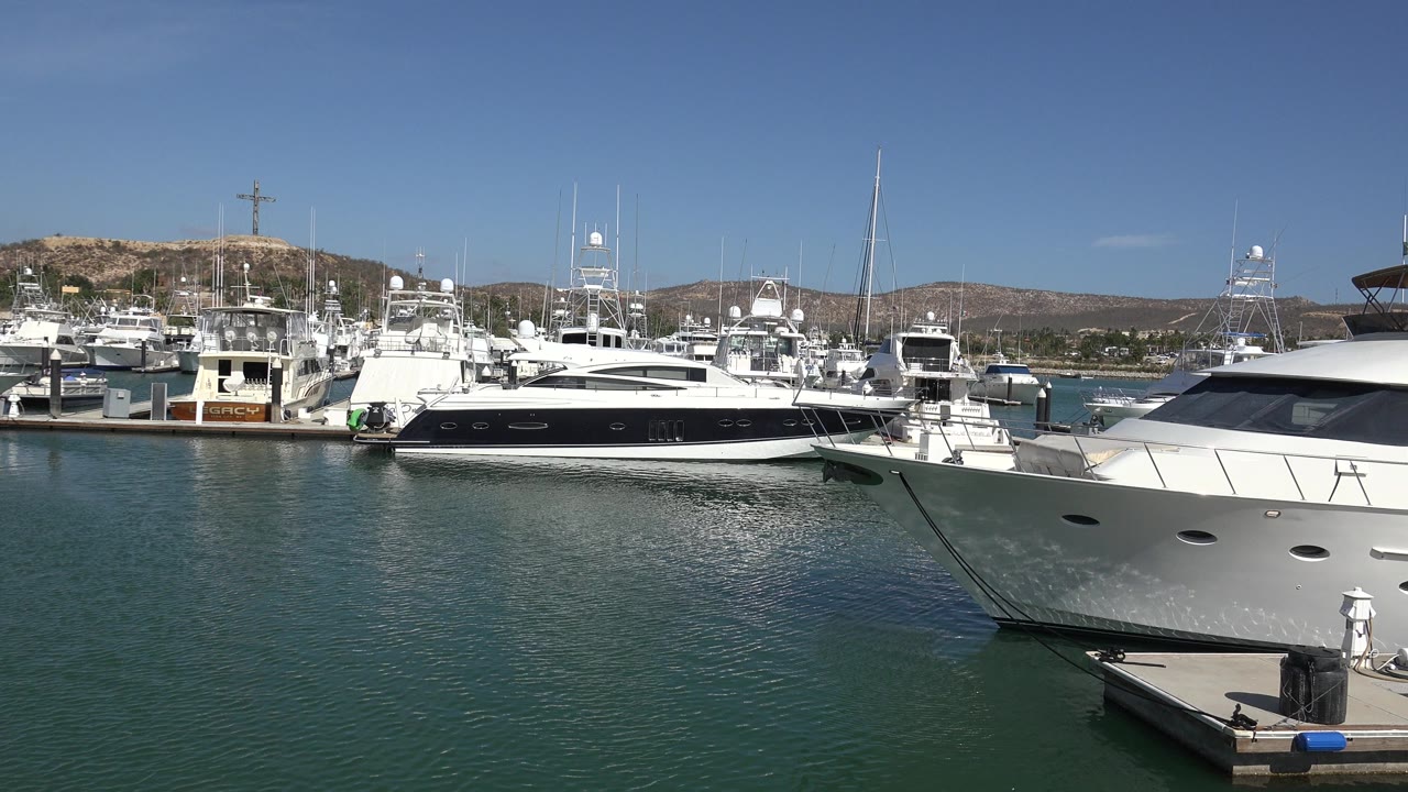 Moored boats in a sunny marina with hills behind them.