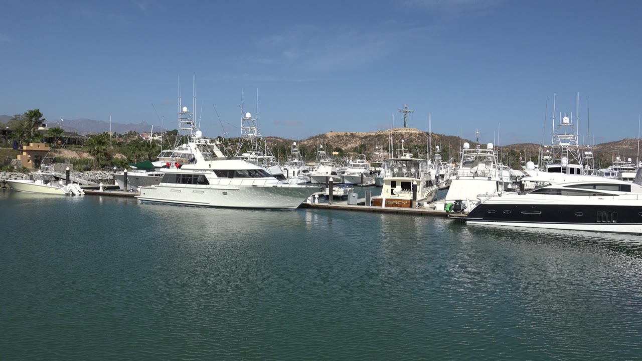 Wide marina view with yachts, docks, calm water, and low hills.