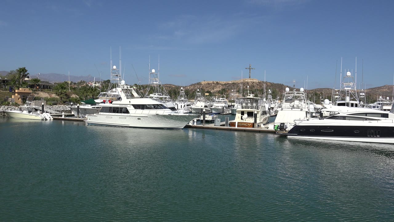San Jose del Cabo marina frame with several docked white boats, dark boat hull at the right edge, bright reflections on the water, and no visible people.