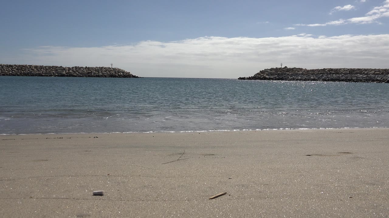 At one second, the San Jose del Cabo shoreline remains clear of people as a thin wave reaches the wet sand below two rock breakwater sections.