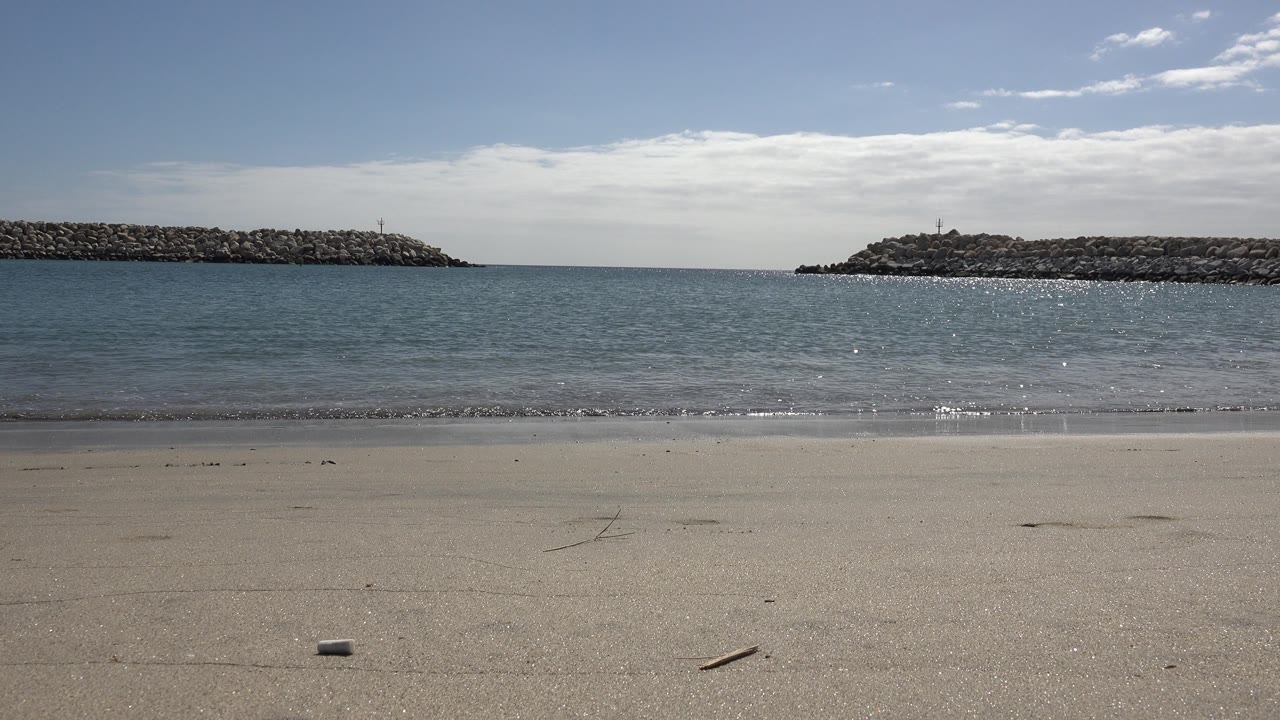 Empty beach and blue green water between two rocky coastal barriers.