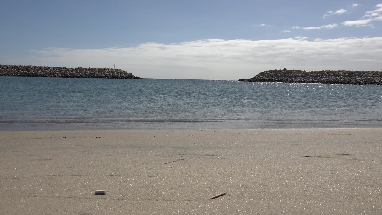 Calm ocean water with sandy foreground and rocks on horizon