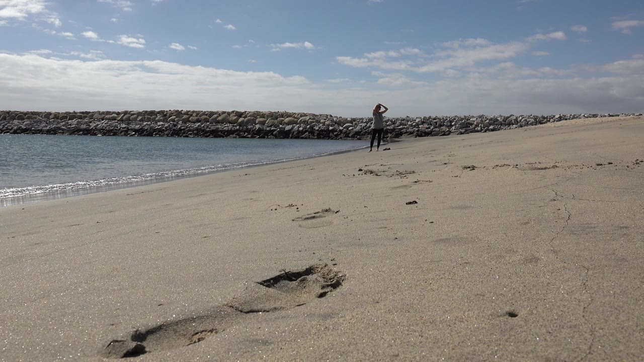wide beach view with a person near the shoreline and a footprint in the sand
