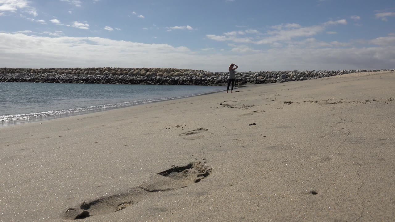 san jose del cabo mexico shoreline with the person still upright near the water a bright strip of small surf at left footprint marks in the sand and the rock outcrop stretching across the background