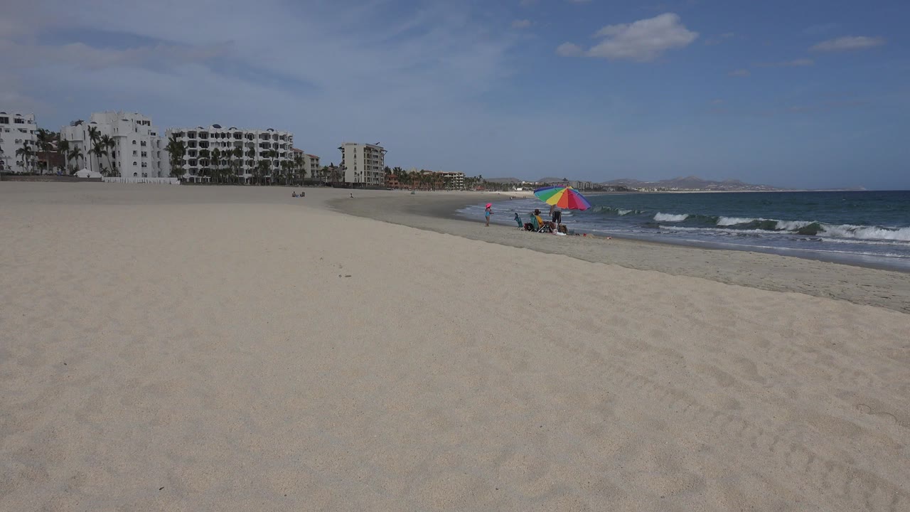 Wide sandy beach with waves, buildings, and a colorful parasol
