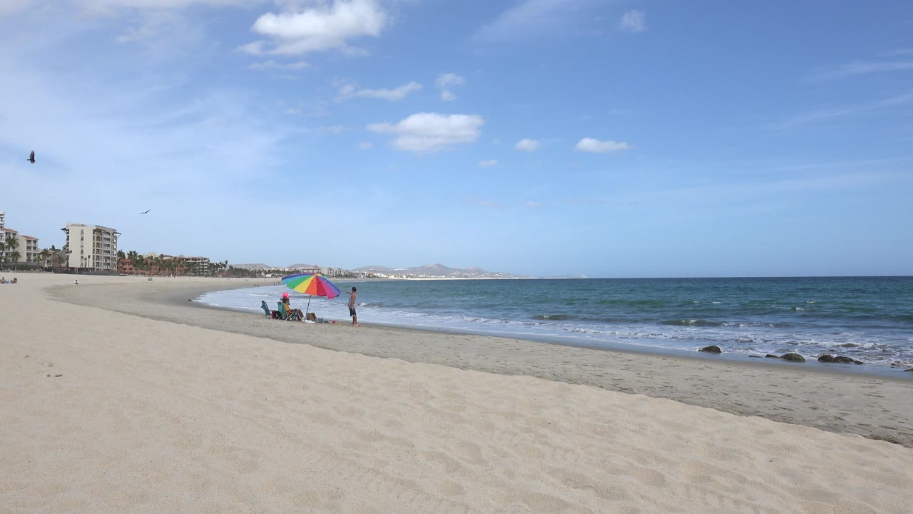 Wide beach with ocean, one colorful umbrella, and distant people near the shore.