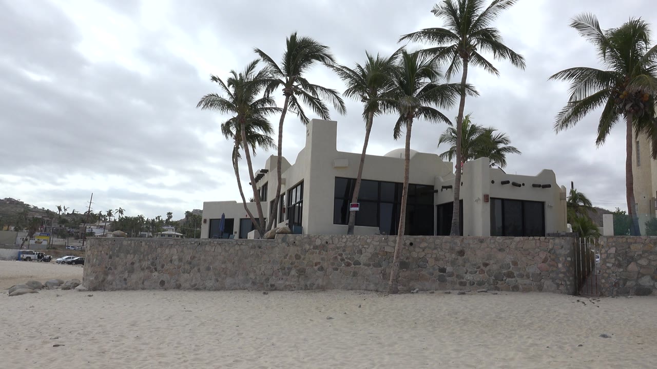 Beach house behind a stone wall with palm trees and sand