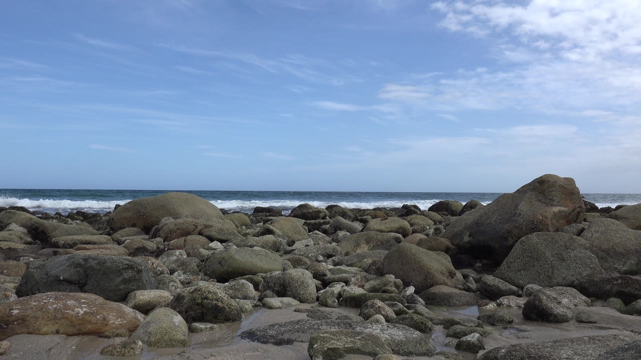 Boulders and surf under a partly clouded sky.