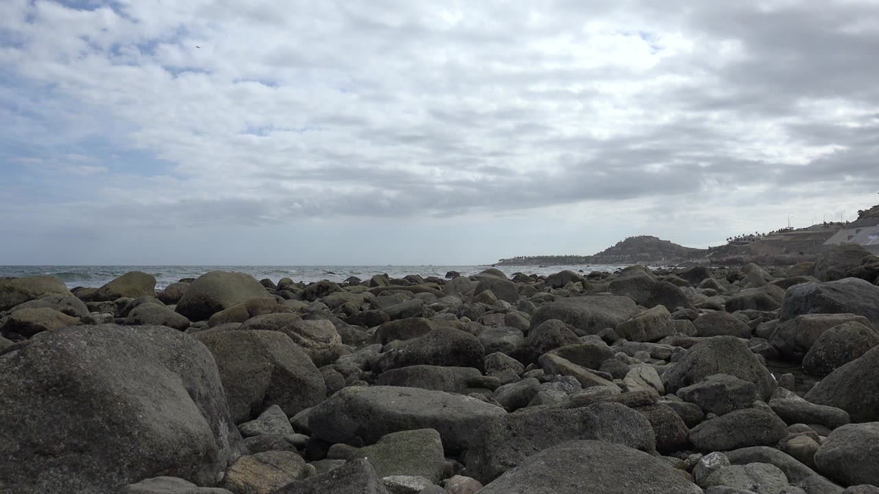 Rocky shoreline under a cloudy sky with ocean surf in the distance.