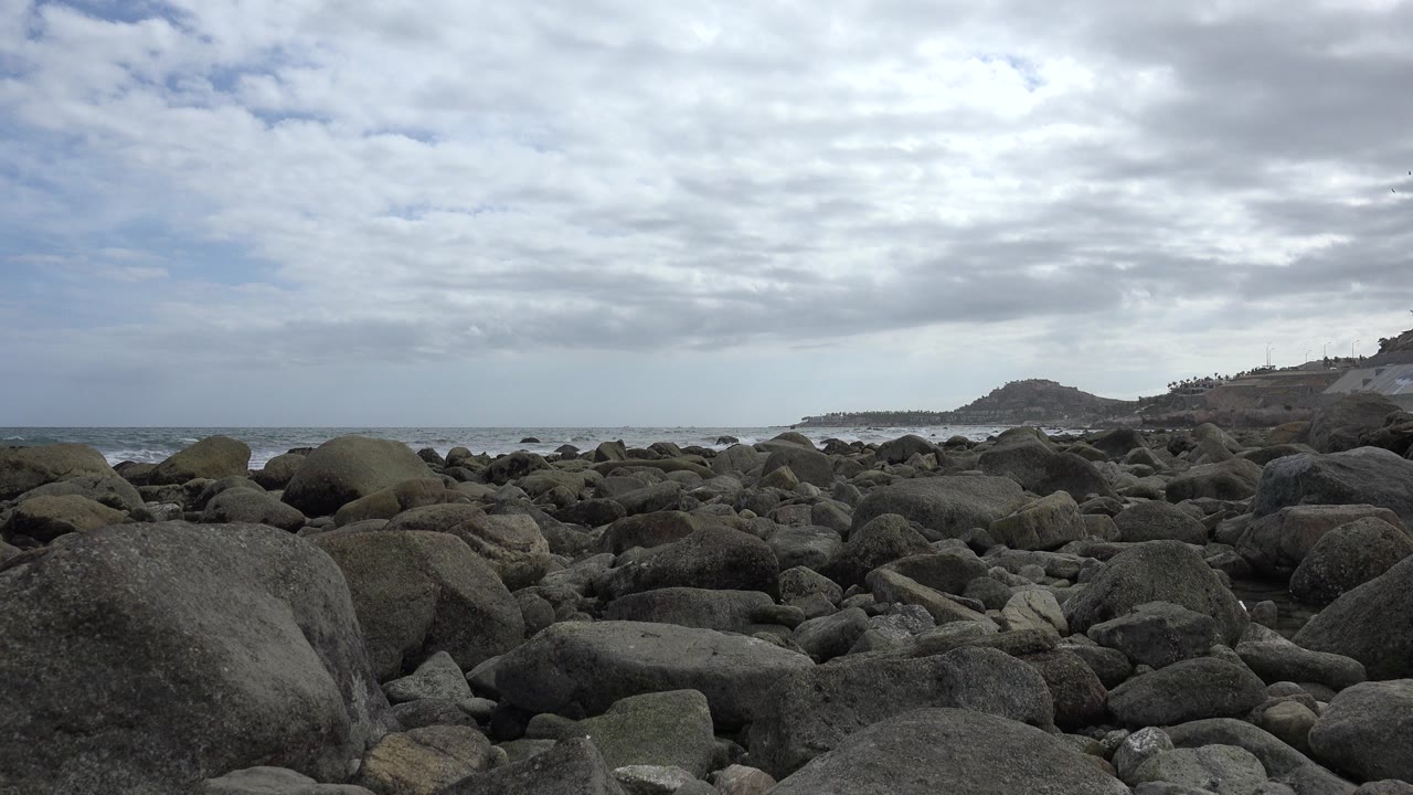 Rocky shoreline under cloudy sky with ocean in the distance.