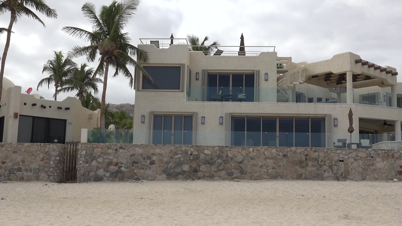 Modern cream beach house behind a stone wall with palms and sand