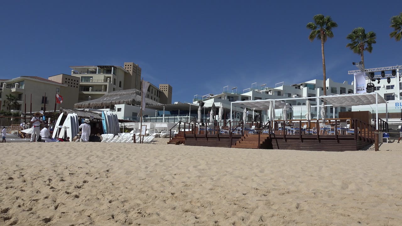 Wide sandy beach in front of a resort deck with palms and umbrellas.