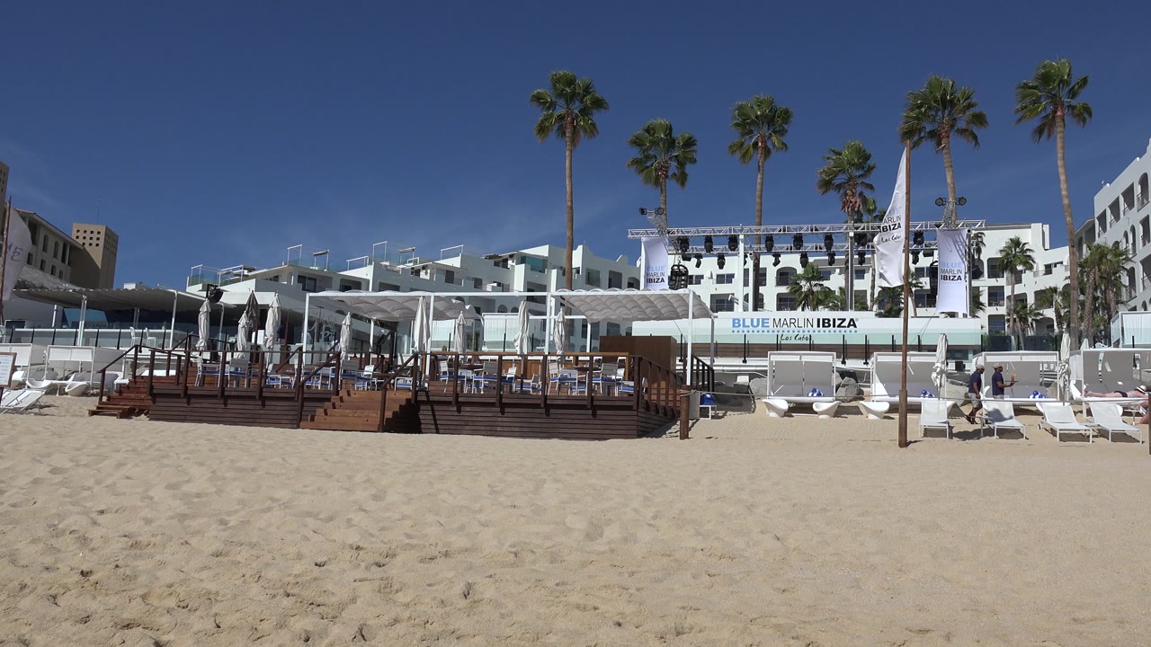 Beach resort deck and white buildings with palms and lounge chairs.