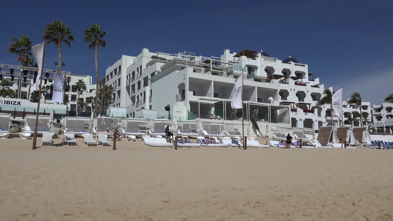 Wide sandy beach facing white waterfront buildings and palm trees.