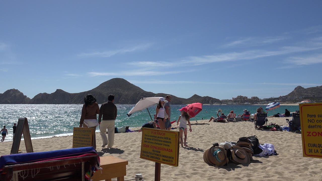 Beachgoers on white sand beside turquoise water and mountain silhouettes.