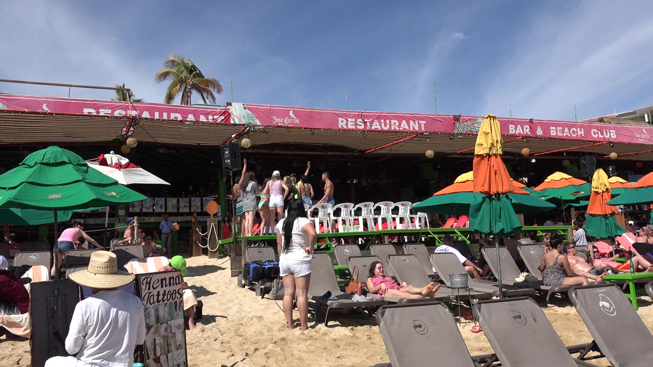 Beach chairs and umbrellas in front of a busy beachside restaurant.