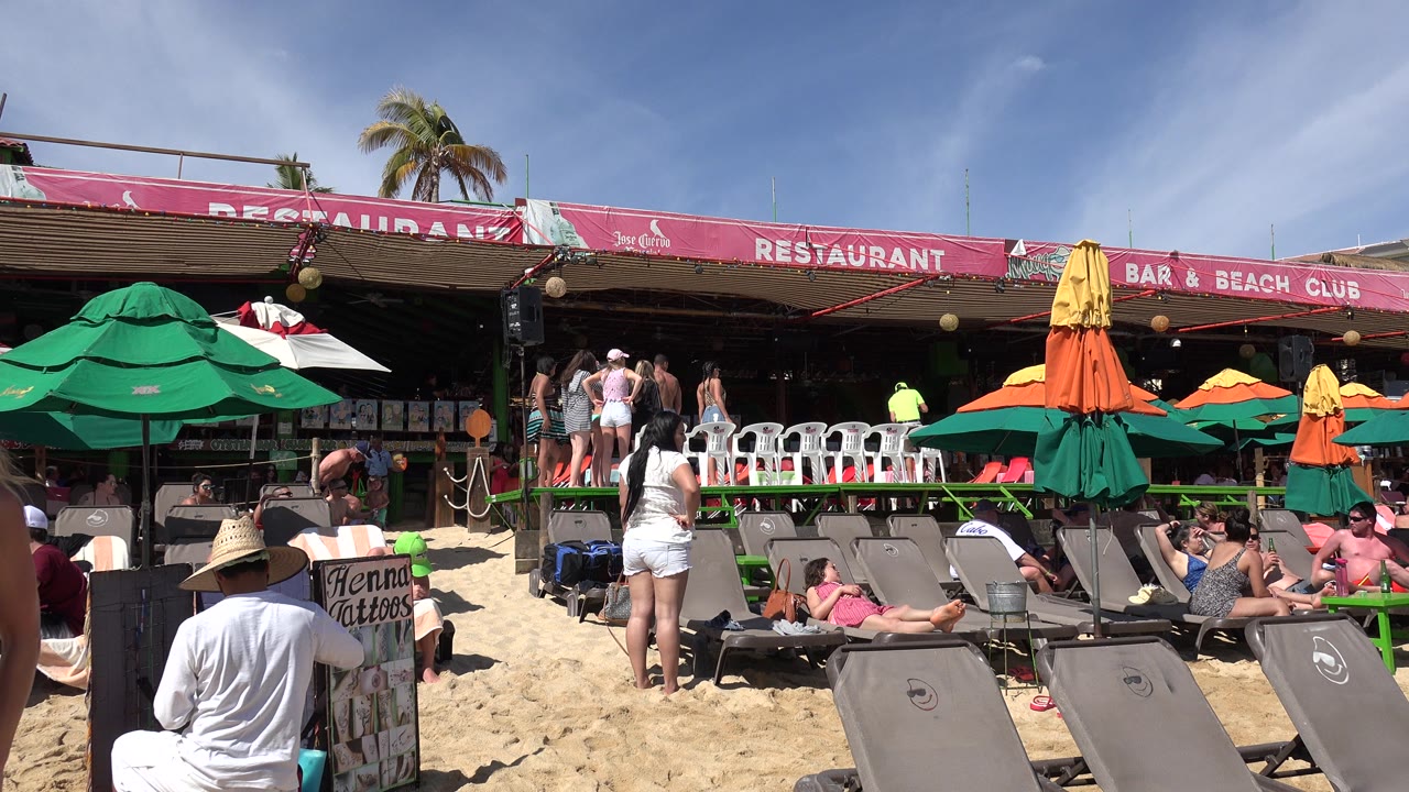 Beach chairs, umbrellas, and people outside a restaurant and bar.