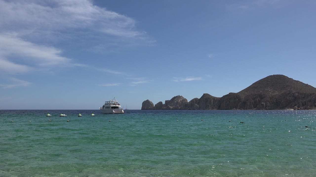 Boat and rocky coastline under a blue sky over green ocean.