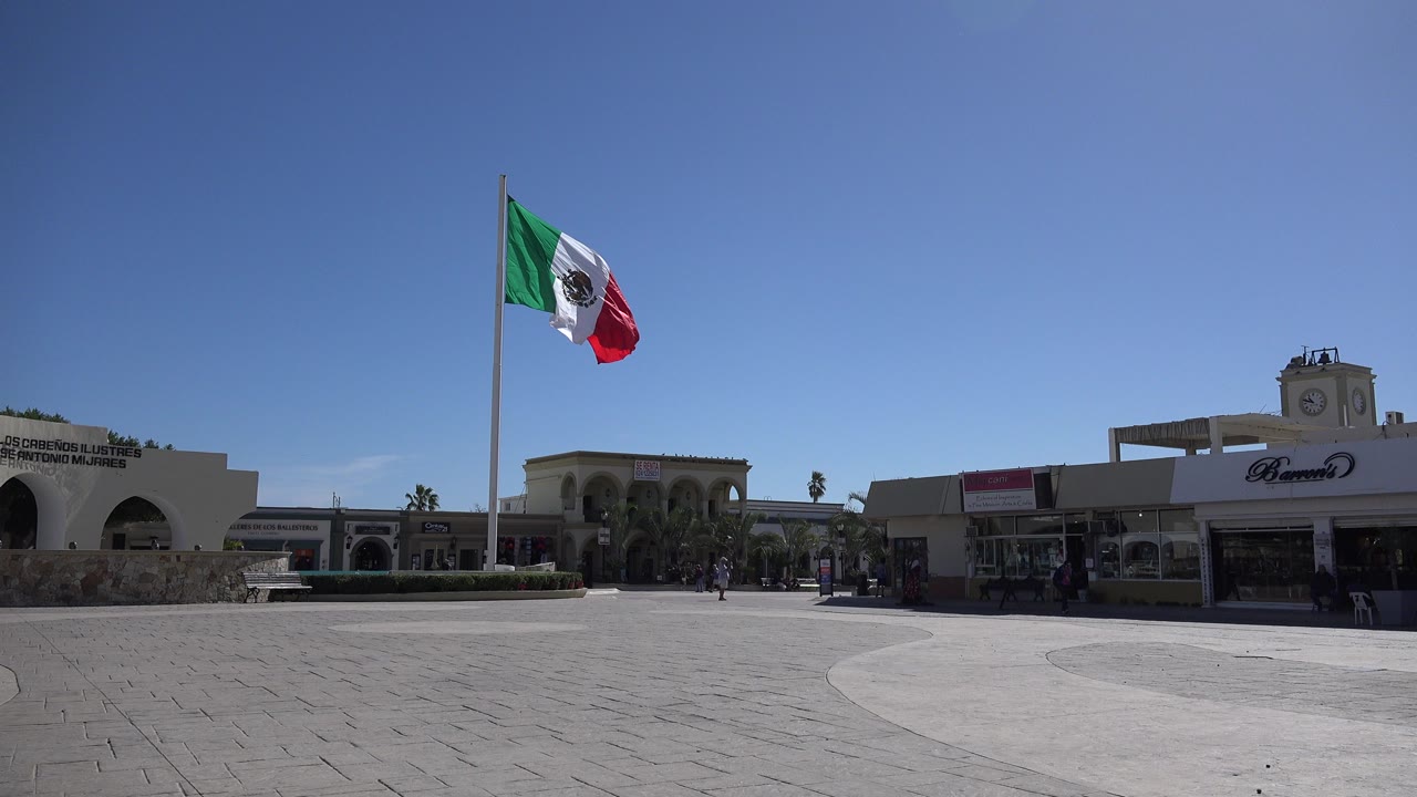 Mexican flag over a paved plaza and low buildings