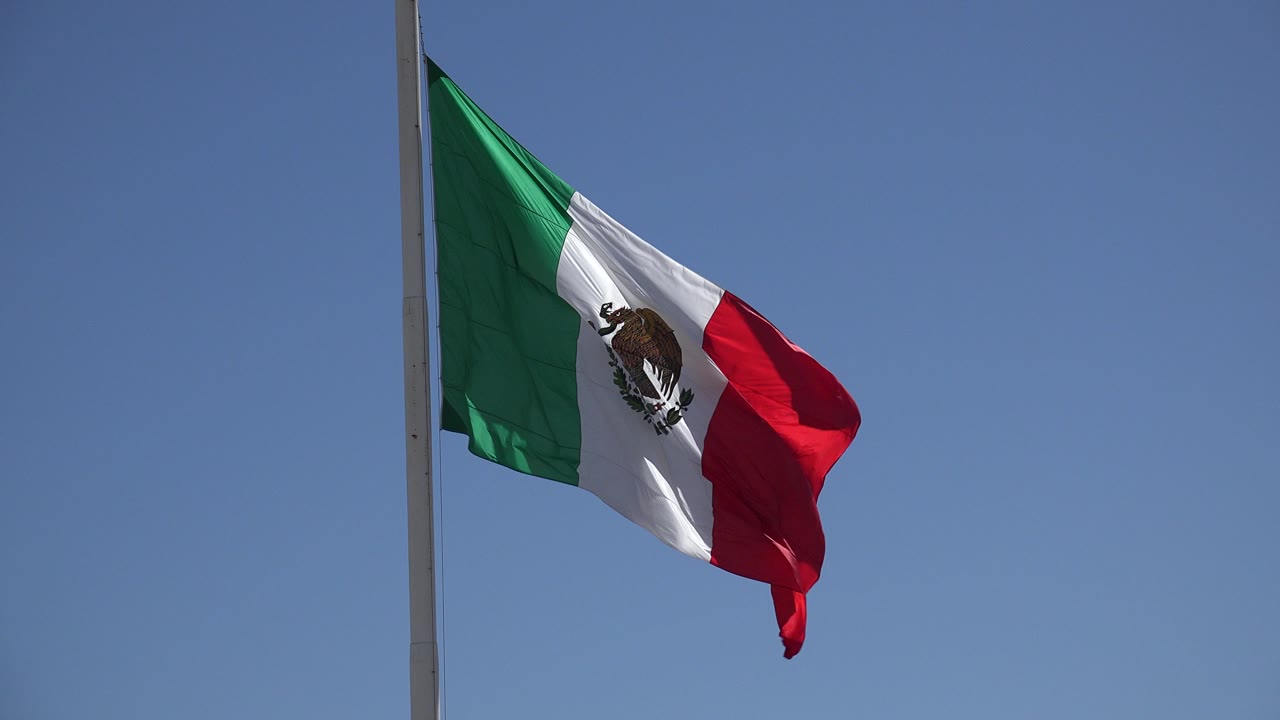 Mexican flag waving on a tall pole against blue sky