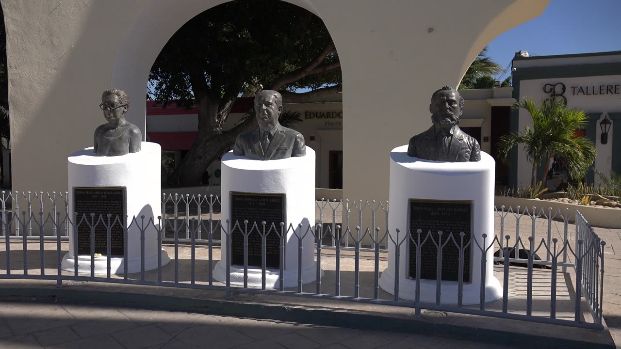 Three busts on white pedestals behind a metal fence