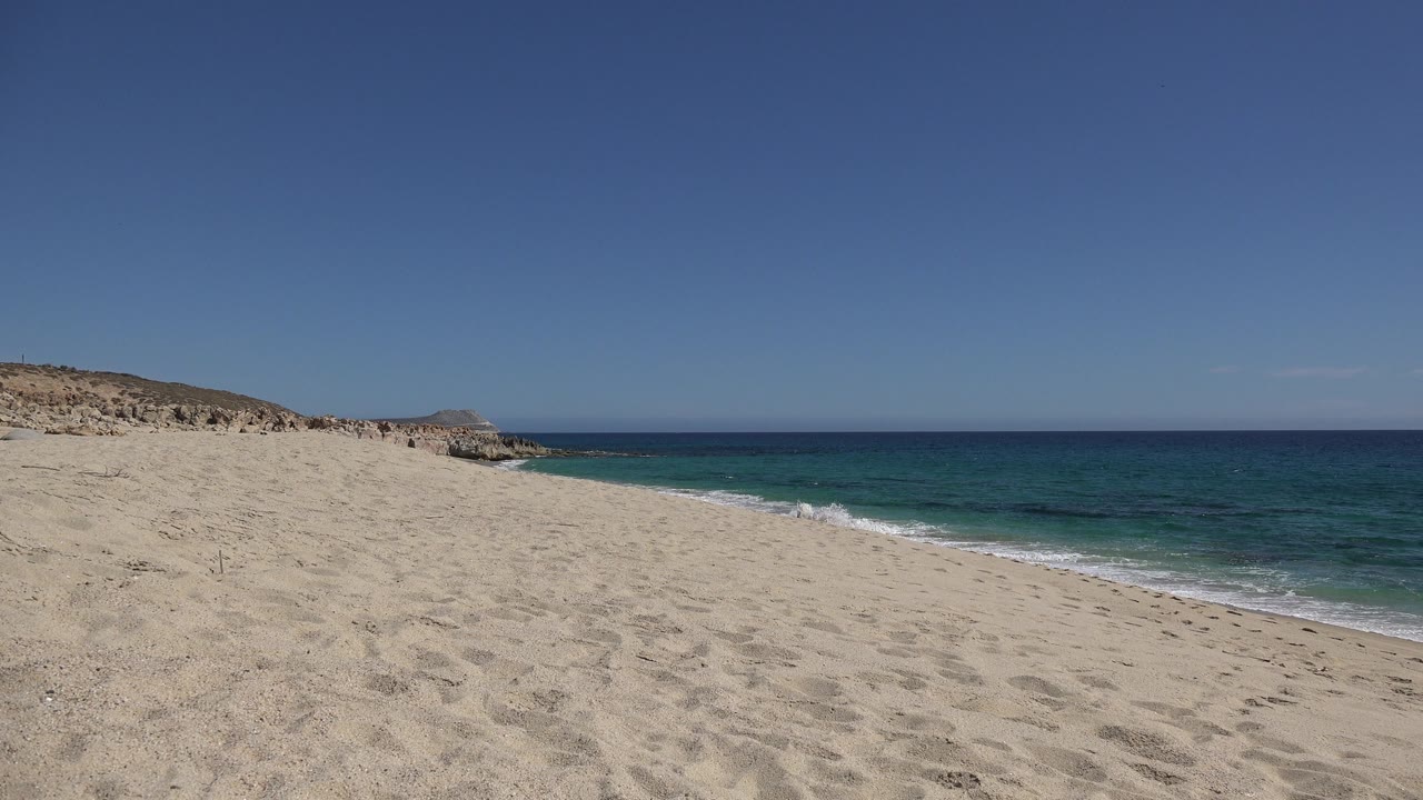 Empty beach with footprints, ocean, and rocky headland