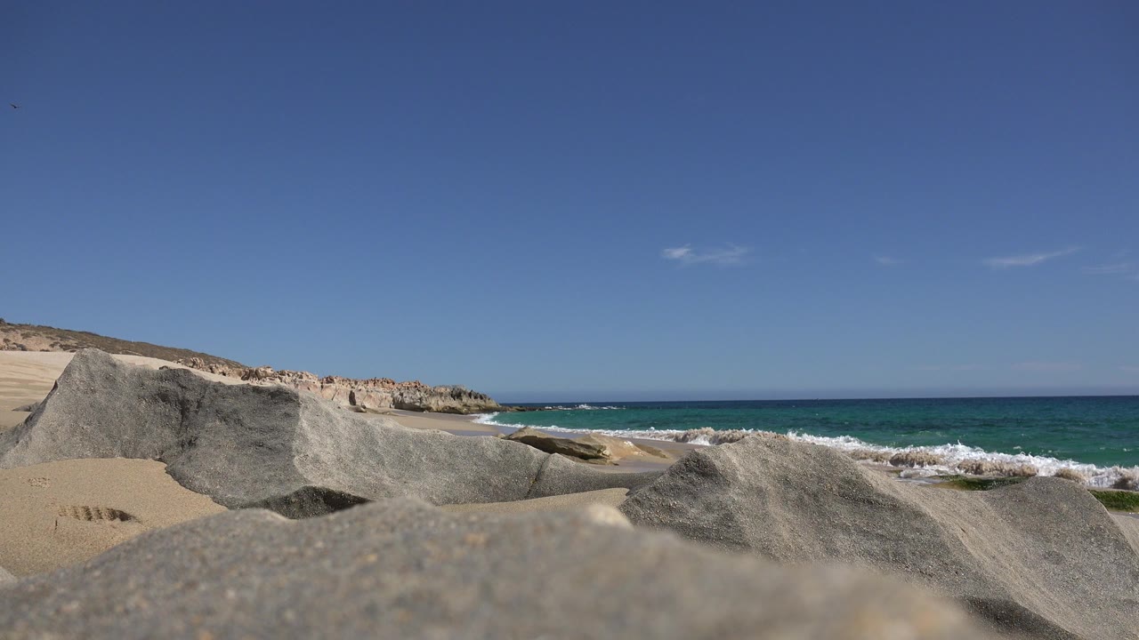 Rocky sandy beach with blue ocean waves and clear sky.