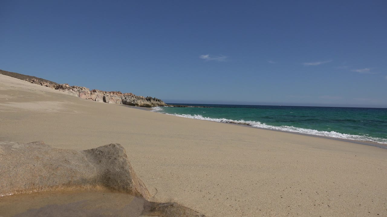 Blue-green ocean beside open sand under clear sky